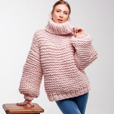 a woman in a pink sweater is posing on a stool with her hand under her chin