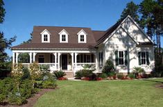 a white house with green shutters on the front and side windows, surrounded by trees