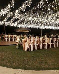 a group of people sitting around a table with white cloths on it at night