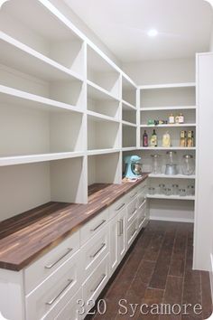 an empty pantry with white cabinets and wood counter tops, along with lots of shelves