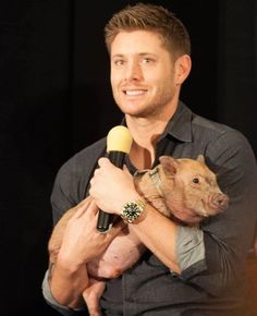 a man holding a small pig in his arms and smiling at the camera while he holds a microphone