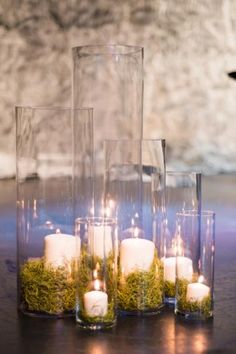 candles are arranged in glass vases with moss on the bottom, and surrounded by greenery