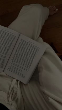 an open book sitting on top of a white bed next to a person's legs