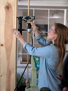 a woman using a power drill to attach a wooden wall hanging on a rope frame