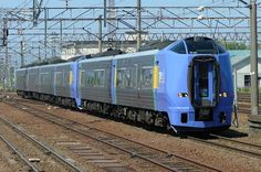 a blue train traveling down tracks next to a building and power lines in the background