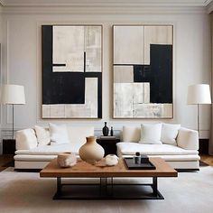 a living room filled with white couches and paintings on the wall above them,