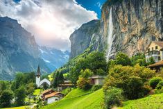 a scenic view of a village in the mountains with a waterfall coming out of it