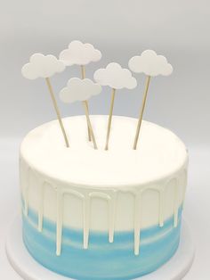 a cake with white icing and blue stripes has clouds on top that have gold sticks sticking out of it