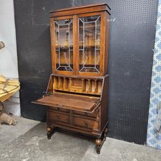 an old wooden desk and hutch with glass doors on the top, sitting in front of a wall