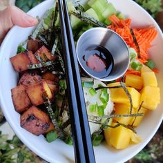 a person holding chopsticks over a bowl of food with vegetables and tofu