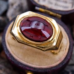 This bold ring features an East-to-West set oval cabochon garnet in a heavy 18k yellow gold mounting with a great patina and a European shank. The garnet has some surface dings and it is lightly cracked but the stone is stable and it is not noticeable when worn. The ring is currently a size 10 and can safely be resized between size 8.5 and 11.5. The ring is currently left unpolished. Formal Cabochon Ruby Ring, Vintage Ruby Ring With Oval Cabochon And Polished Finish, Vintage Oval Cabochon Ruby Ring With Polished Finish, Vintage Red Signet Ring With Oval Cabochon, Formal Domed Signet Ring With Cabochon, Vintage Red Oval Cabochon Signet Ring, Vintage Oval Cabochons For Formal Occasions, Modernist Formal Cabochon Rings, Gold Ruby Ring With Bezel Setting, Oval Cabochon