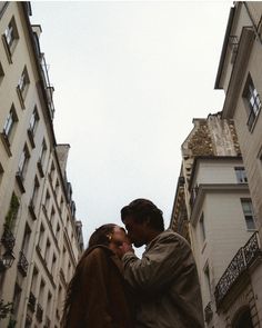 a man and woman kissing in between two tall buildings