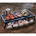 an outdoor grill with hamburgers and hot dogs cooking on it's side in the grass