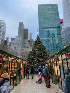 people are walking down the sidewalk in front of christmas trees and tall buildings with lights on them