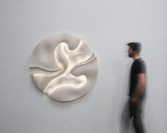 a man standing next to a white wall with a sculpture on it's side