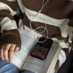 a person sitting down reading a book and listening to music with headphones on their ears