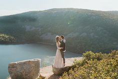 a man and woman standing on top of a cliff next to a body of water