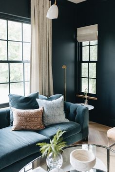 a living room with black walls and blue couches in the corner, along with two windows that have drapes on them