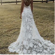 the back of a woman's white wedding dress with flowers on it, standing in an open field