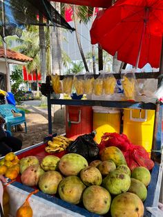 there are many different fruits on display at the market table with umbrellas over them