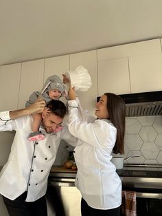 a man and woman holding a child in the air while standing next to an oven