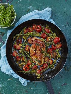 a skillet filled with meat and vegetables on top of a blue cloth next to a bowl of green beans