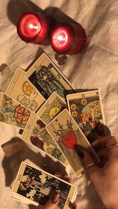 a person holding tarot cards in their hands with two red candles on the table