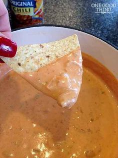 a hand holding a tortilla chip over a bowl of chili and cheese dip