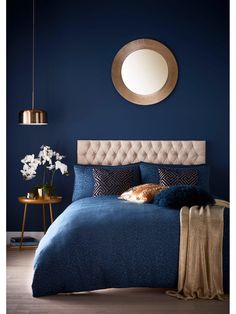 a bed with blue sheets and pillows in front of a round mirror on the wall