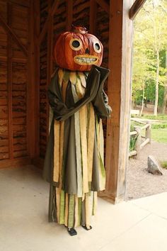 a scarecrow with a pumpkin on his head standing in front of a wooden building