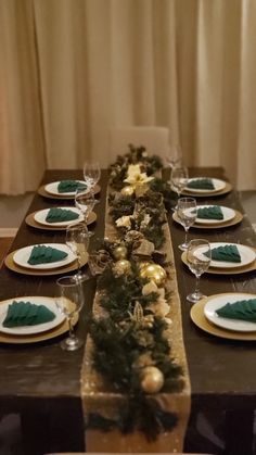 the table is set with green and gold plates, silverware, and greenery