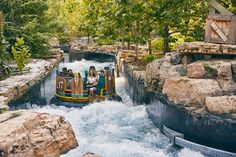 people are riding on a water ride in the middle of a river surrounded by rocks and trees