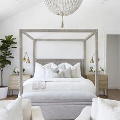 a white bedroom with four poster bed and two couches in front of the bed