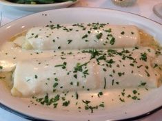 two burritos covered in white sauce and garnished with parsley on a plate