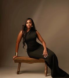 a woman in a black dress is sitting on a bench and posing for the camera