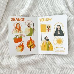 an open book with pictures of people and symbols in orange on the cover, sitting on a white blanket