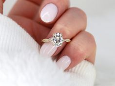 a woman's hand holding a ring with a diamond on it and white sweater