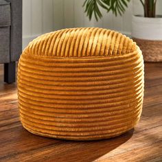 a large yellow round ottoman sitting on top of a wooden floor next to a potted plant