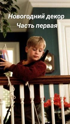 a young boy standing on top of a balcony next to a potted plant and holding a cell phone