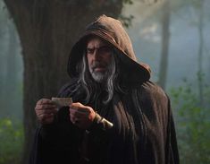 an old man with long gray hair holding a knife and looking at something in his hand