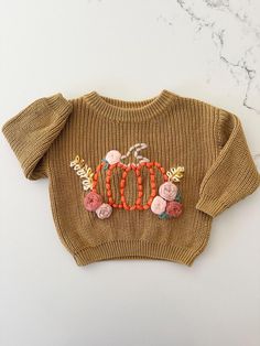 a brown sweater with flowers and buttons on the front is sitting on a marble surface