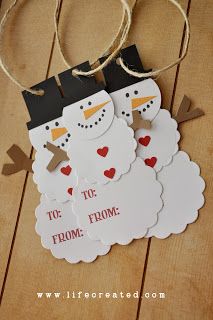 two snowmen standing next to each other on top of a wooden floor with tags