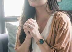 a woman sitting on a couch with her hands clasped in front of her chest and looking off into the distance