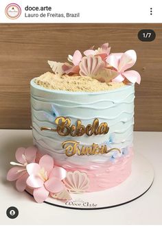 the cake is decorated with pink and blue icing, flowers, and gold lettering