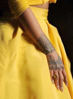 a woman in a yellow dress with tattoos on her arm and hand, wearing a ring