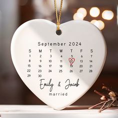 a white heart shaped ornament with a date on it and a tiny spider sitting next to it