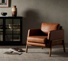 a brown leather chair sitting on top of a rug next to a book case and vase