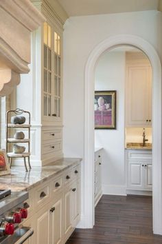 a kitchen with white cabinets and wood flooring next to an archway leading into the dining room