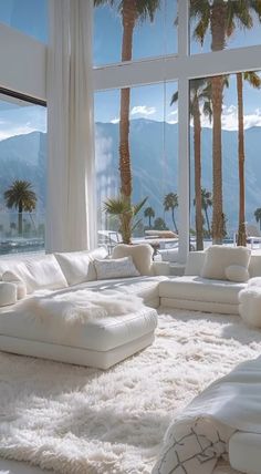 a living room filled with lots of white furniture and palm trees in the window sill