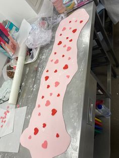 a pink cake with hearts on it sitting on top of a metal counter next to other items